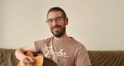 Smiling man holding a guitar, promoting the Guitar for Beginners community.